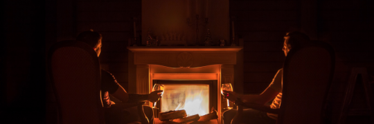 alt="two people sitting in front of a fireplace"